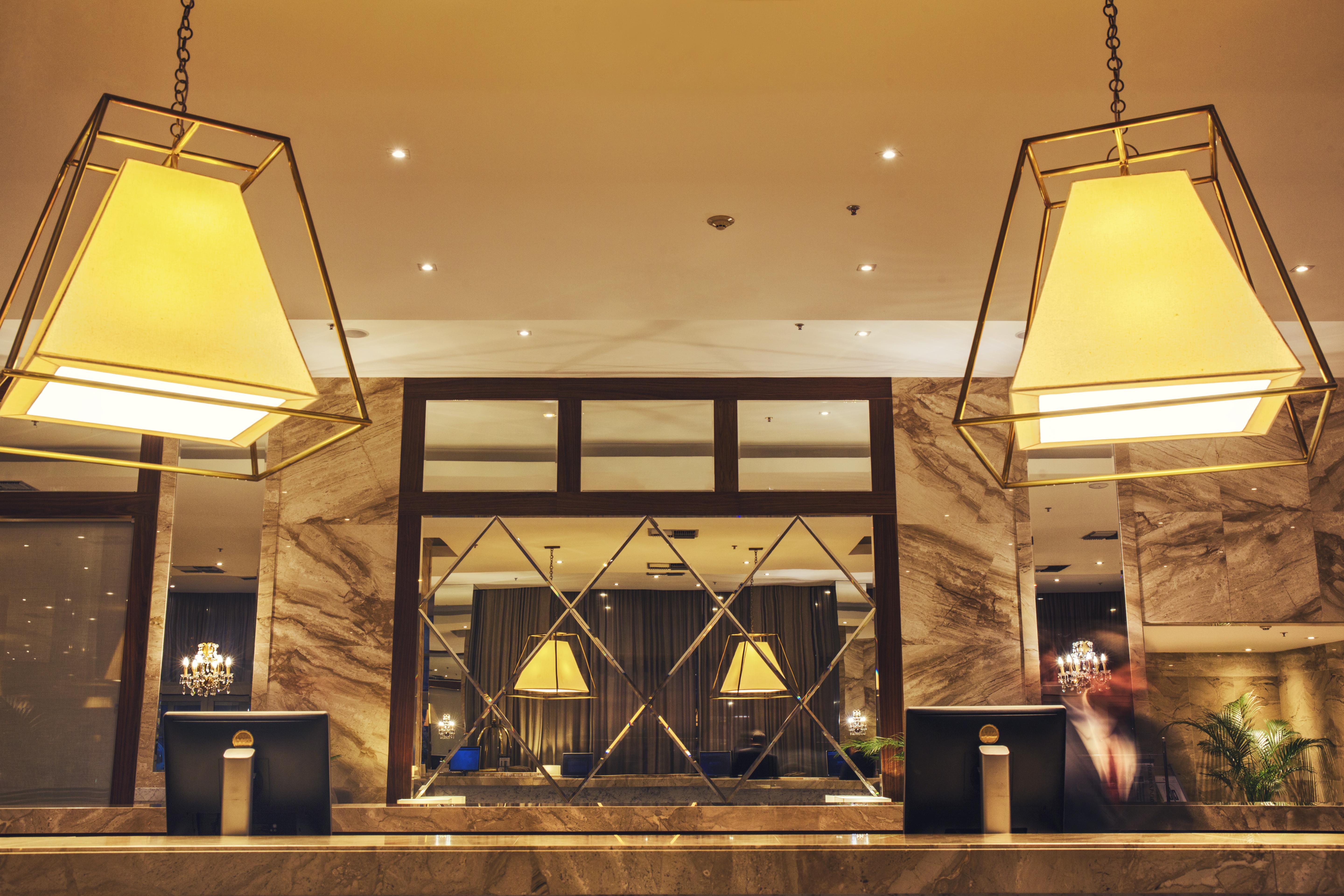 Windsor Marapendi Hotel Rio de Janeiro Eksteriør bilde The photo shows a hotel lobby or reception area. There are large geometric light fixtures hanging from the ceiling, providing a warm glow to the space. The reception desk is made of a polished material, likely marble, with decorative elements and two